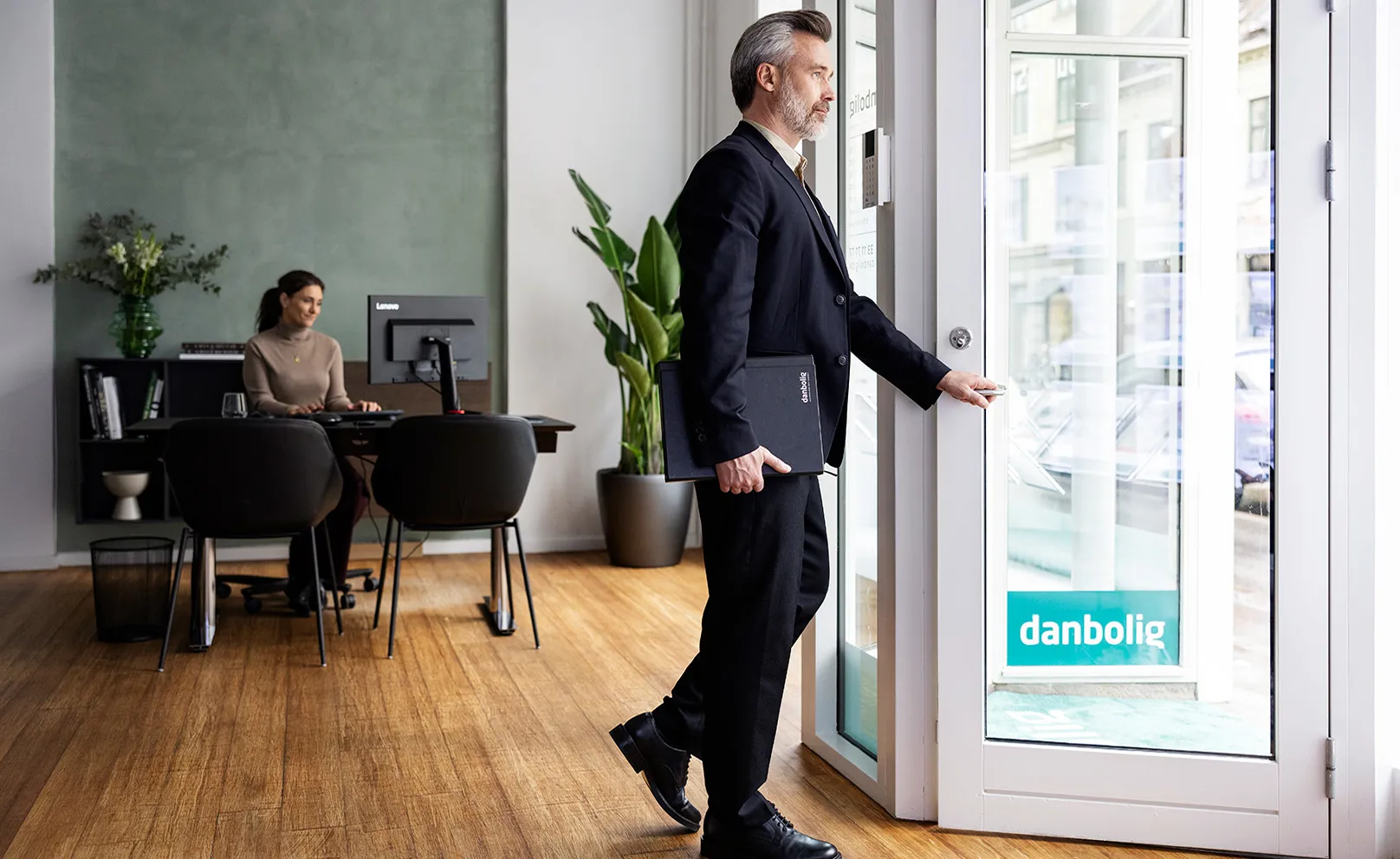 Ejendomsmægler i jakkesæt med laptop og kaffe åbner dør i danbolig-kontor