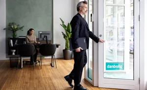 Ejendomsmægler i jakkesæt med laptop og kaffe åbner dør i danbolig-kontor