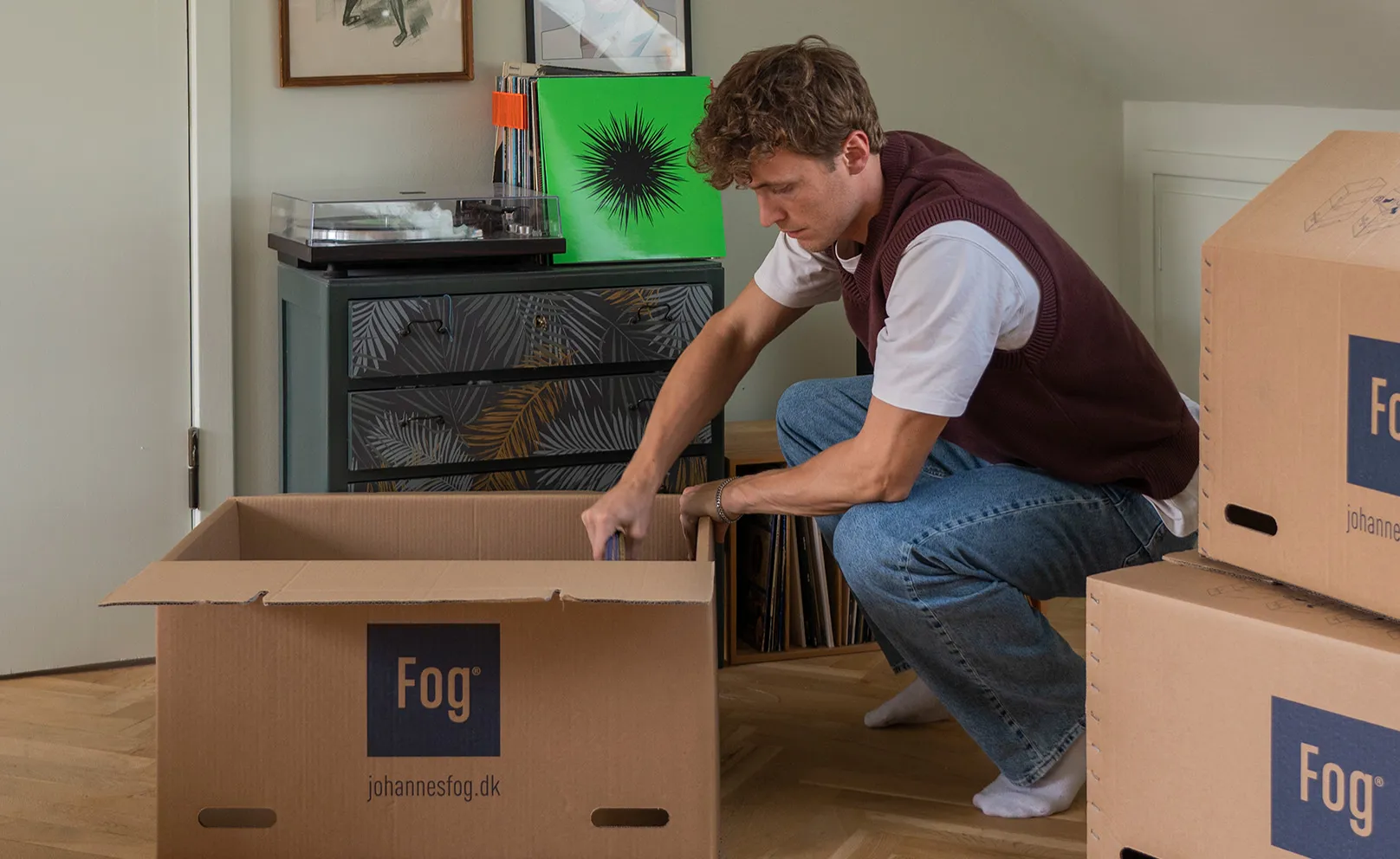 Ung mand sidder p&#xE5; hug og putter b&#xF8;ger i en flyttekasse
