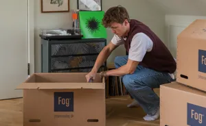 Ung mand sidder på hug og putter bøger i en flyttekasse