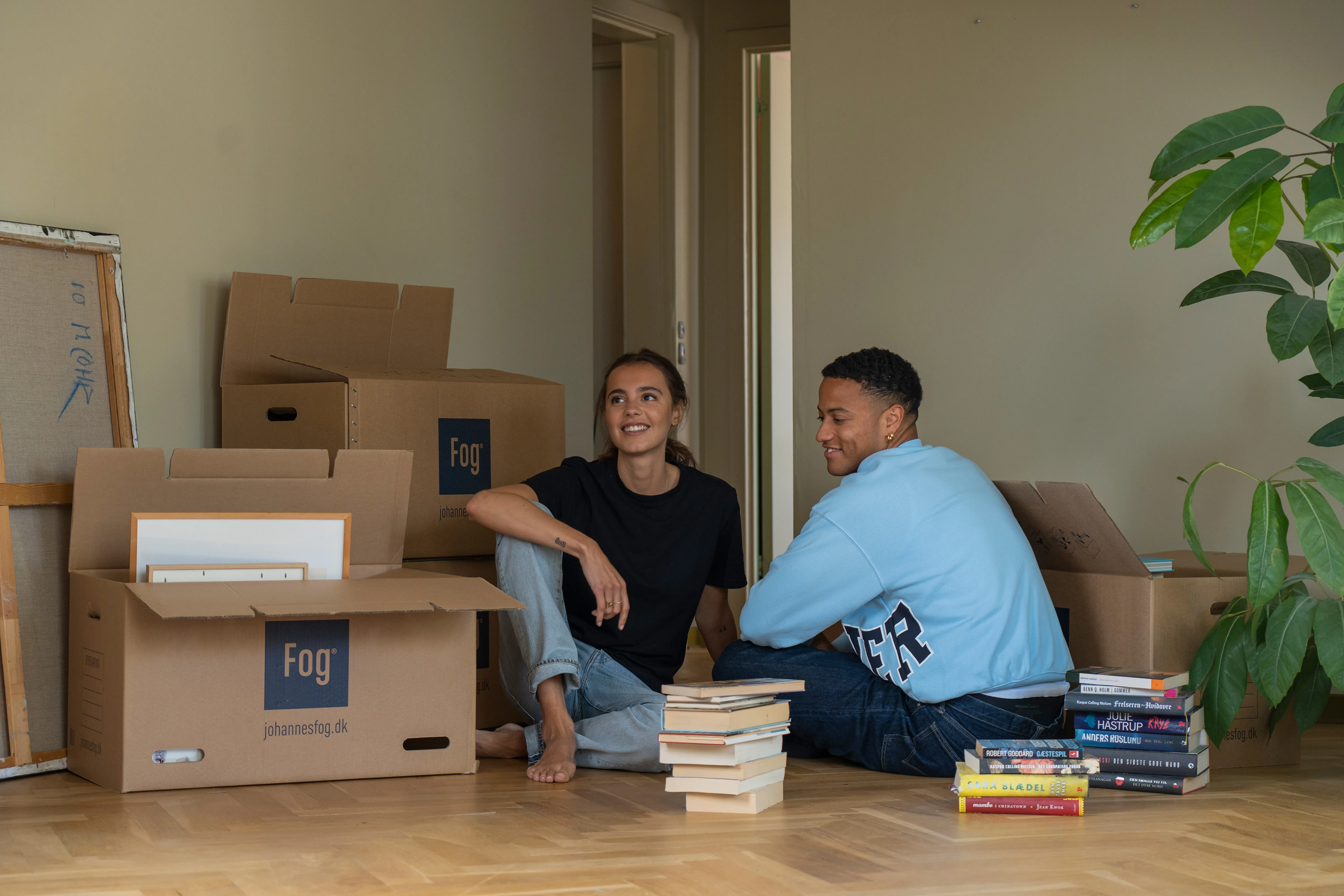 To unge mennesker sidder på gulvet omkranset af flyttekasser