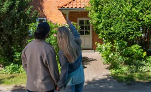 Par står foran murstensvilla med hvid dør og peger