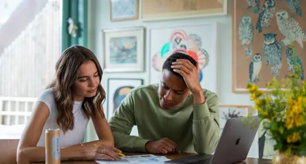 To unge mennesker sidder med computer og kigger i papirer ved spisebord