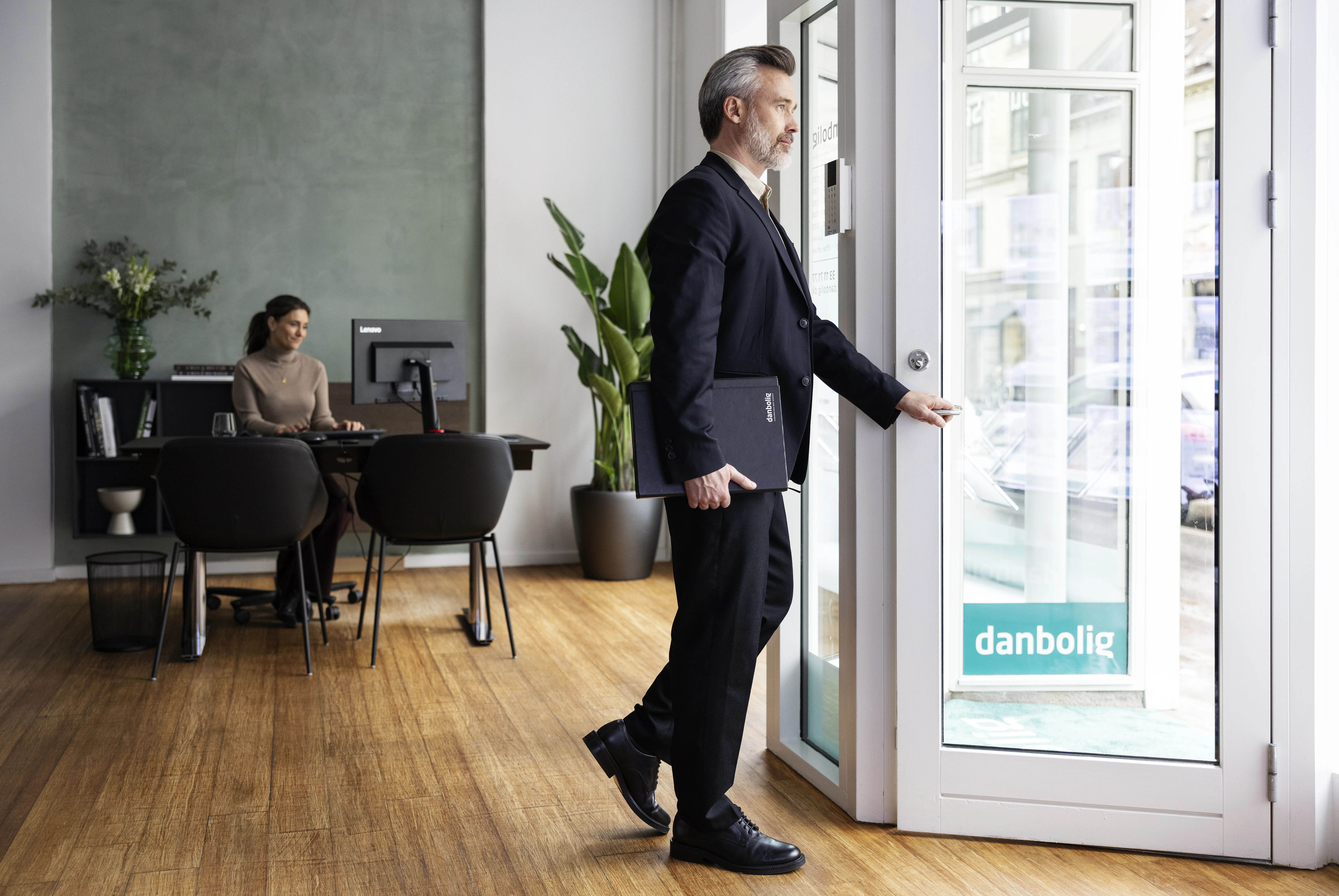 Ejendomsmægler i jakkesæt med laptop og kaffe åbner dør i danbolig-kontor