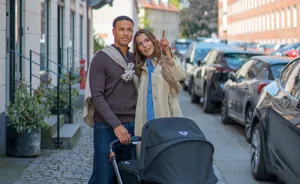 Ungt par går med barnevogn og peger på boliger på vejen