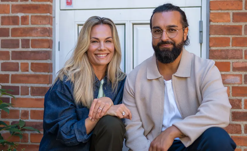 To personer sidder foran villa og smiler