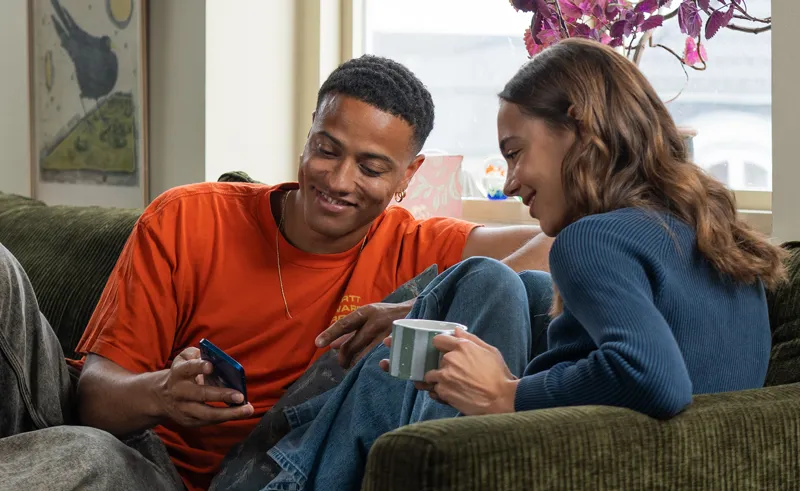 To unge mennesker sidder i sofa og kigger på en telefon