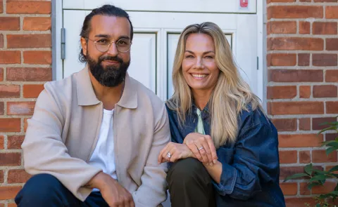 To personer sidder foran villa og smiler 