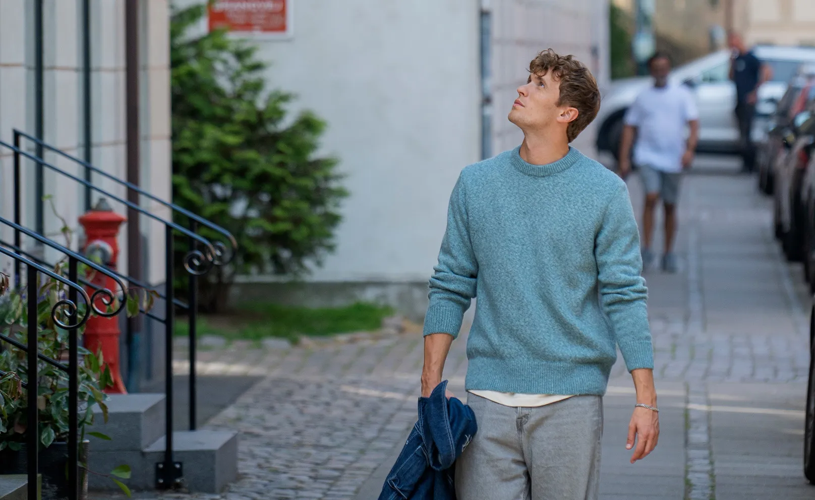 Ung mand med sin jakke i hånden går på gade og kigger op på lejligheder