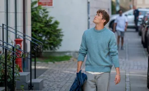 Ung mand med sin jakke i hånden går på gade og kigger op på lejligheder