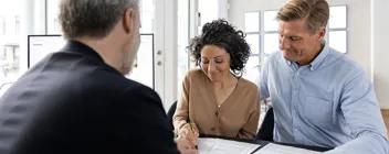 To personer er til møde med ejendomsmægler, hvor kvinde underskriver dokument