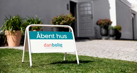 Skilt fra danbolig med “Åbent hus” foran hus med åben dør og blomster