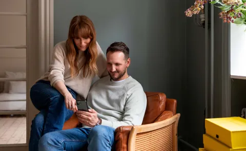 To personer sidder i brun lænestol og kigger på en mobiltelefon