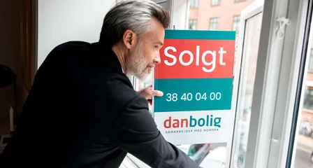 Ejendomsmægler sætter "Solgt"-skilt fra danbolig i vinduet i en lejlighed