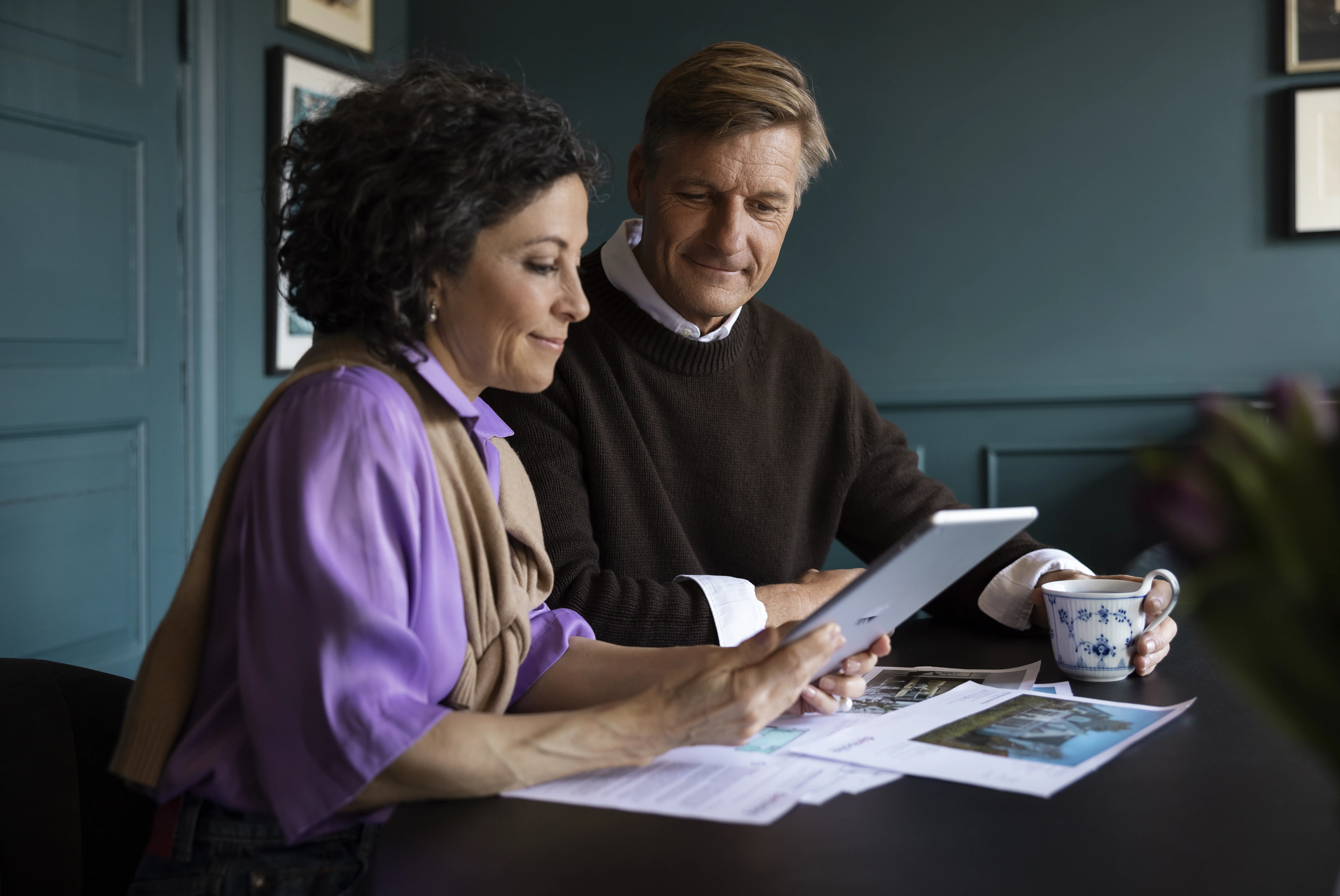 To personer i boligrådgivning hos danbolig sidder ved bord med tablet, kaffekop og papirer
