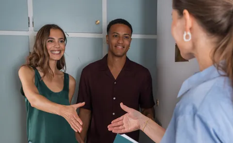 Ejendomsmægler hilser på unge boligejere i døråbningen i lejlighed