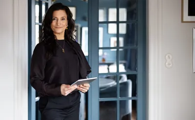 Ejendomsmægler står med iPad foran glasdører i en bolig