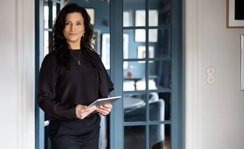 Ejendomsmægler står med iPad foran glasdører i en bolig