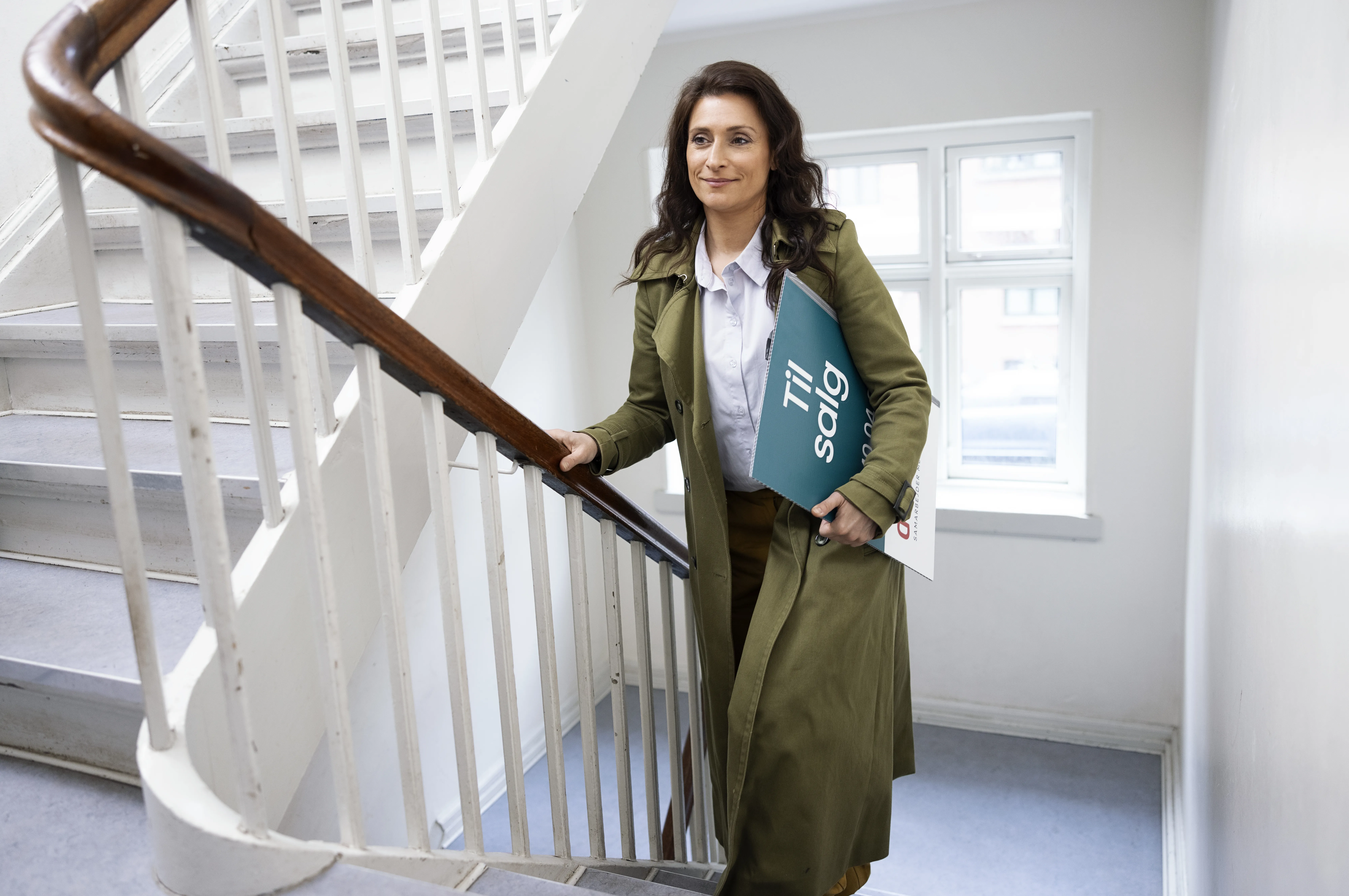 Ejendomsmægler går op ad trappe med et "Til salg"-skilt under armen