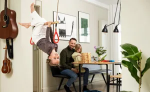 Barn svinger i trapez i dørkarmen, mens far kigger på i baggrunden