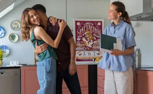 Ungt par krammer hinanden, mens ejendomsmægler smiler