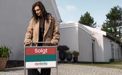 Ejendomsmægler fra danbolig sætter "Solgt"-skilt i jorden foran hus