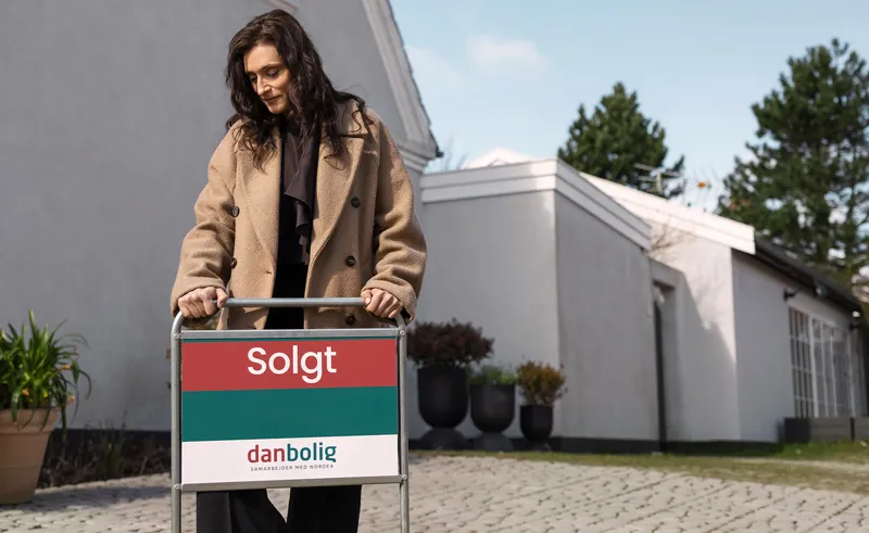 Ejendomsmægler fra danbolig sætter "Solgt"-skilt i jorden foran hus