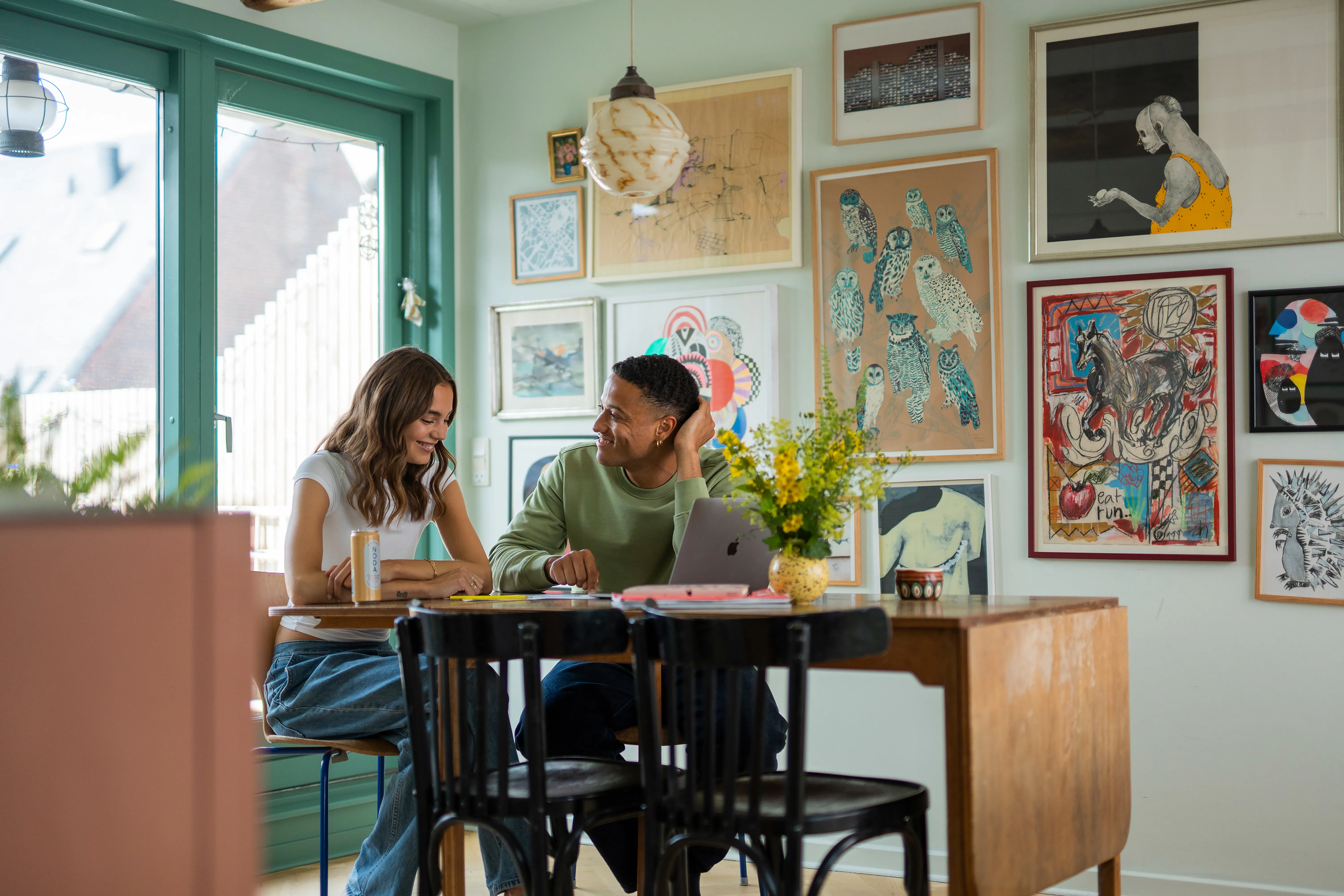 To unge mennesker sidder ved spisebord og griner