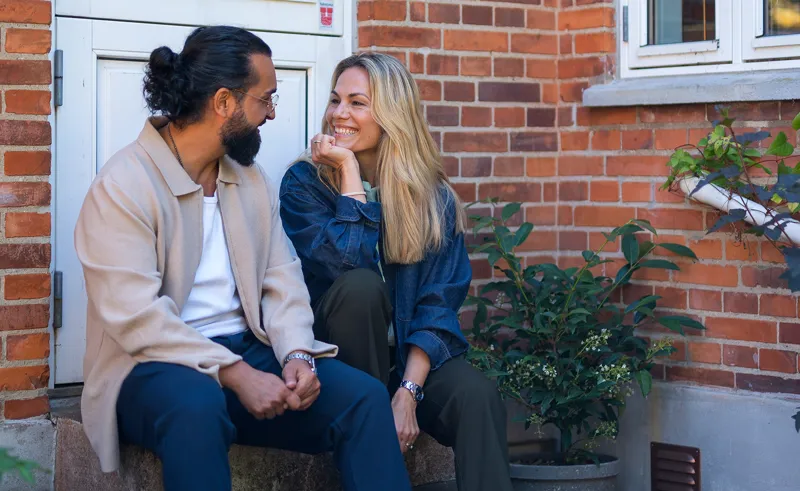 Par sidder på trappe foran villa og smiler til hinanden