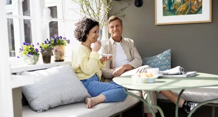Par sidder på bænk og smiler med en kop kaffe