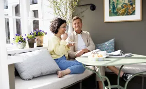 Par sidder på bænk og smiler med en kop kaffe
