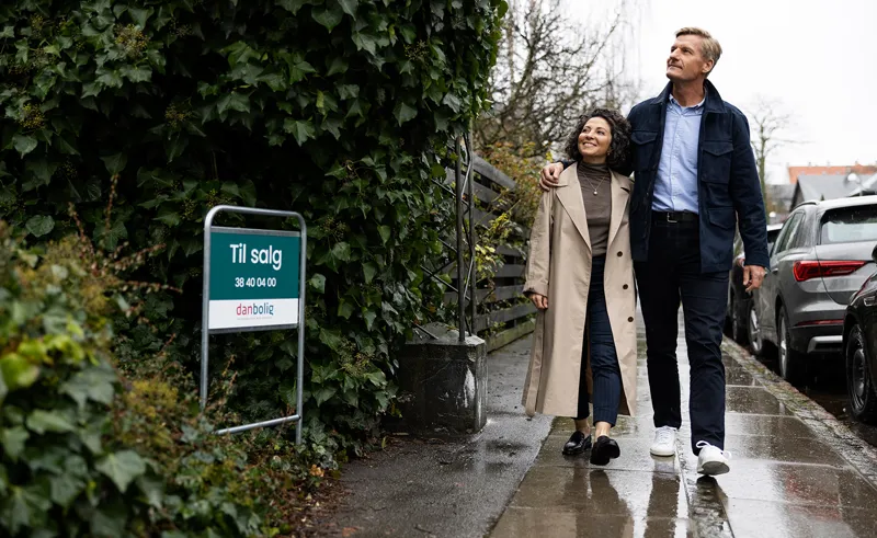 Par går på en villavej forbi et "Til salg"-skilt fra danbolig