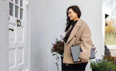 Ejendomsmægler med mappe under armen står ved hoveddøren til hus