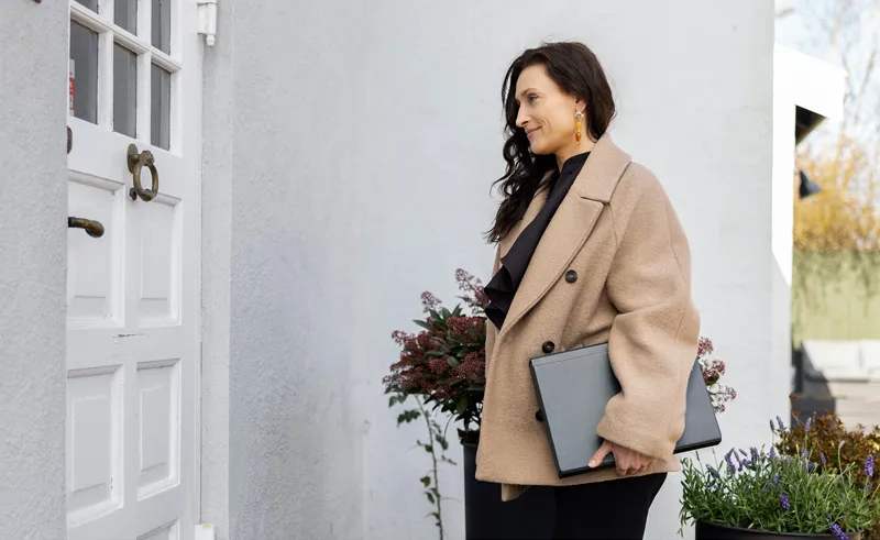 Ejendomsmægler med mappe under armen står ved hoveddøren til hus