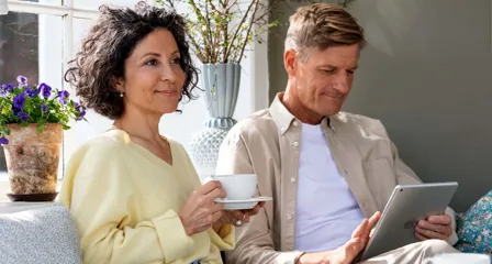 To personer i hyggelig stue, én med tablet og én med kaffekop